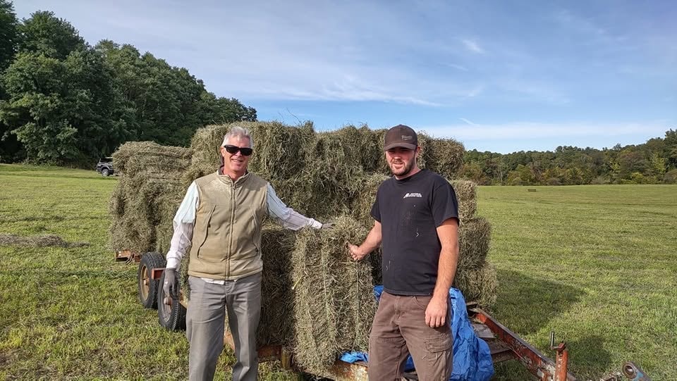 Two men posing with hay bales on the farm